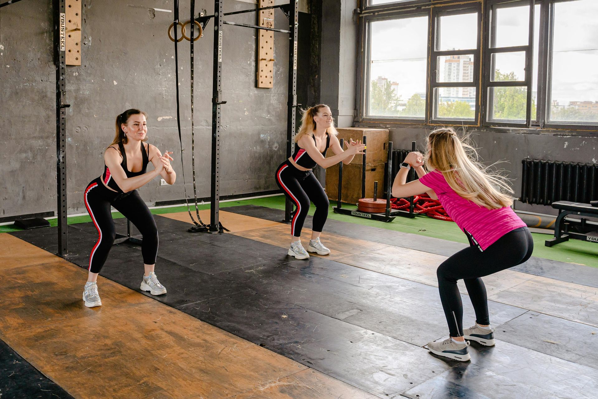 Three women are doing squats in a gym.