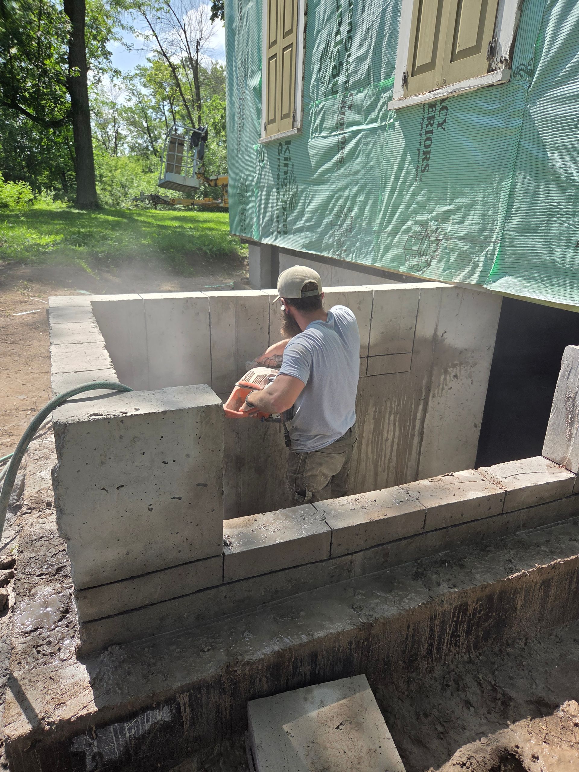 A person uses a circular saw to cut a concrete block wall at a residential construction site.