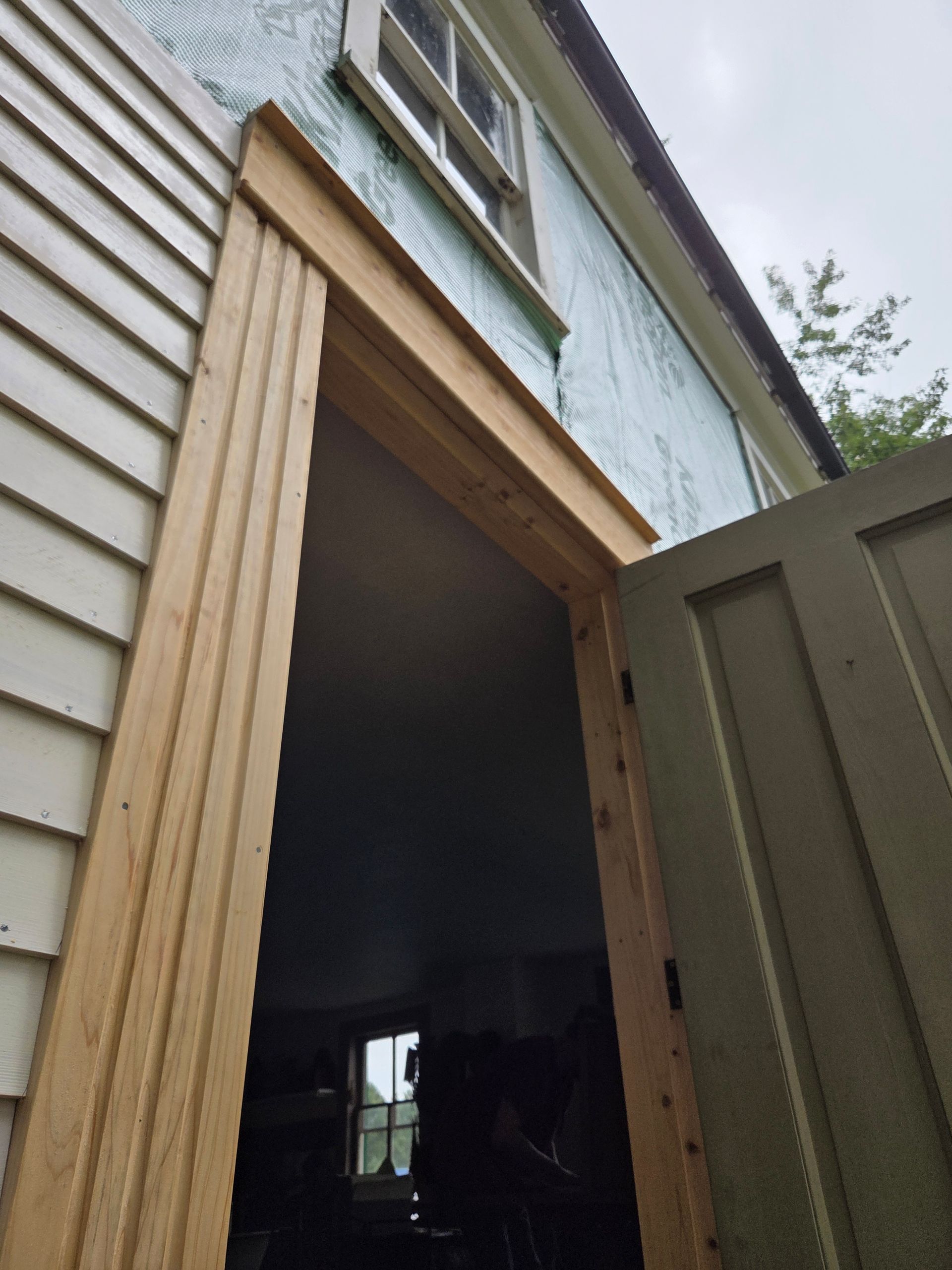 A low-angle view shows an open exterior doorway with new, light-colored wood trim framing, set against light blue siding.