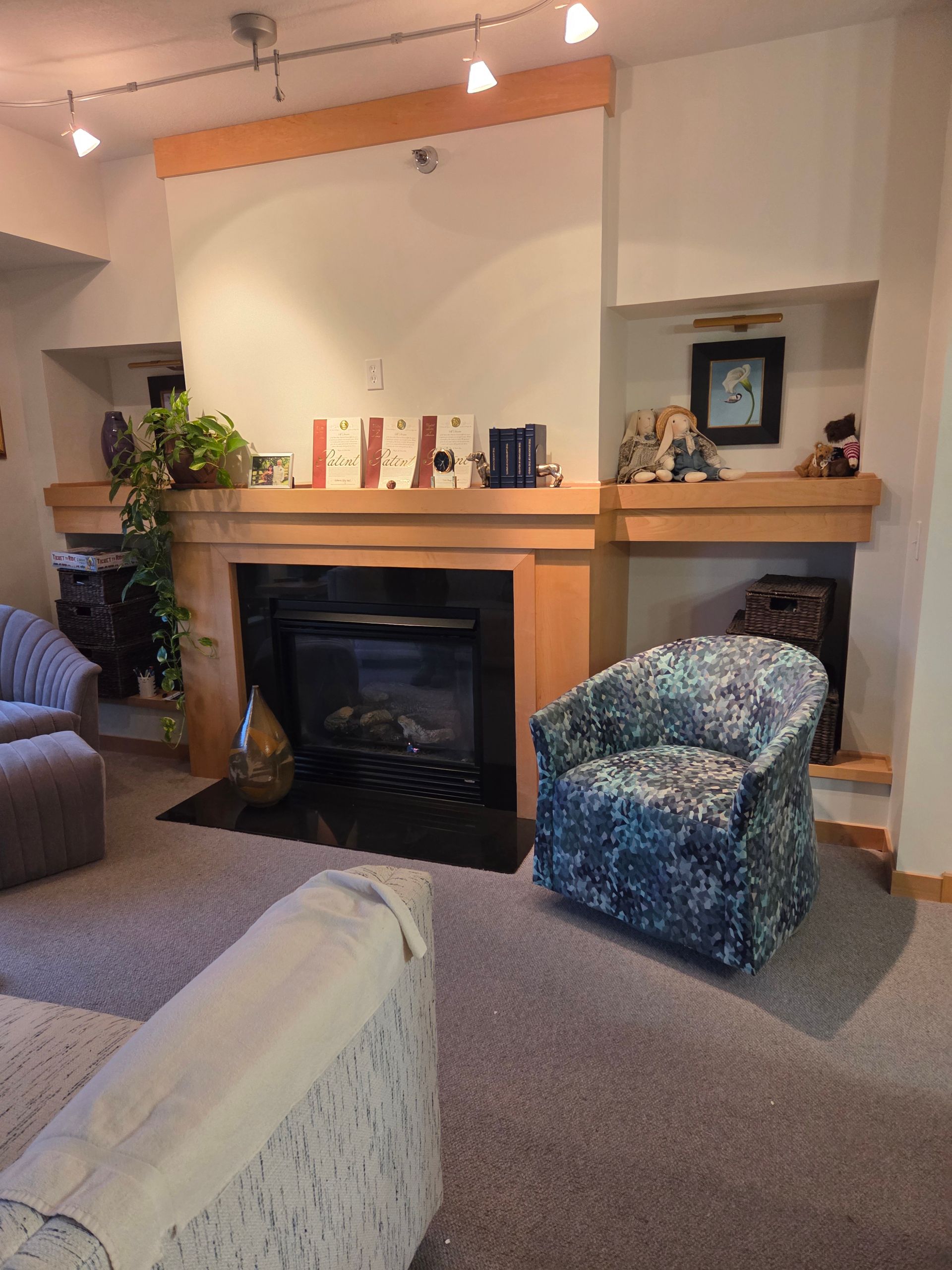 A living room with a fireplace, a patterned blue armchair, a cream sofa, and track lighting on the ceiling.