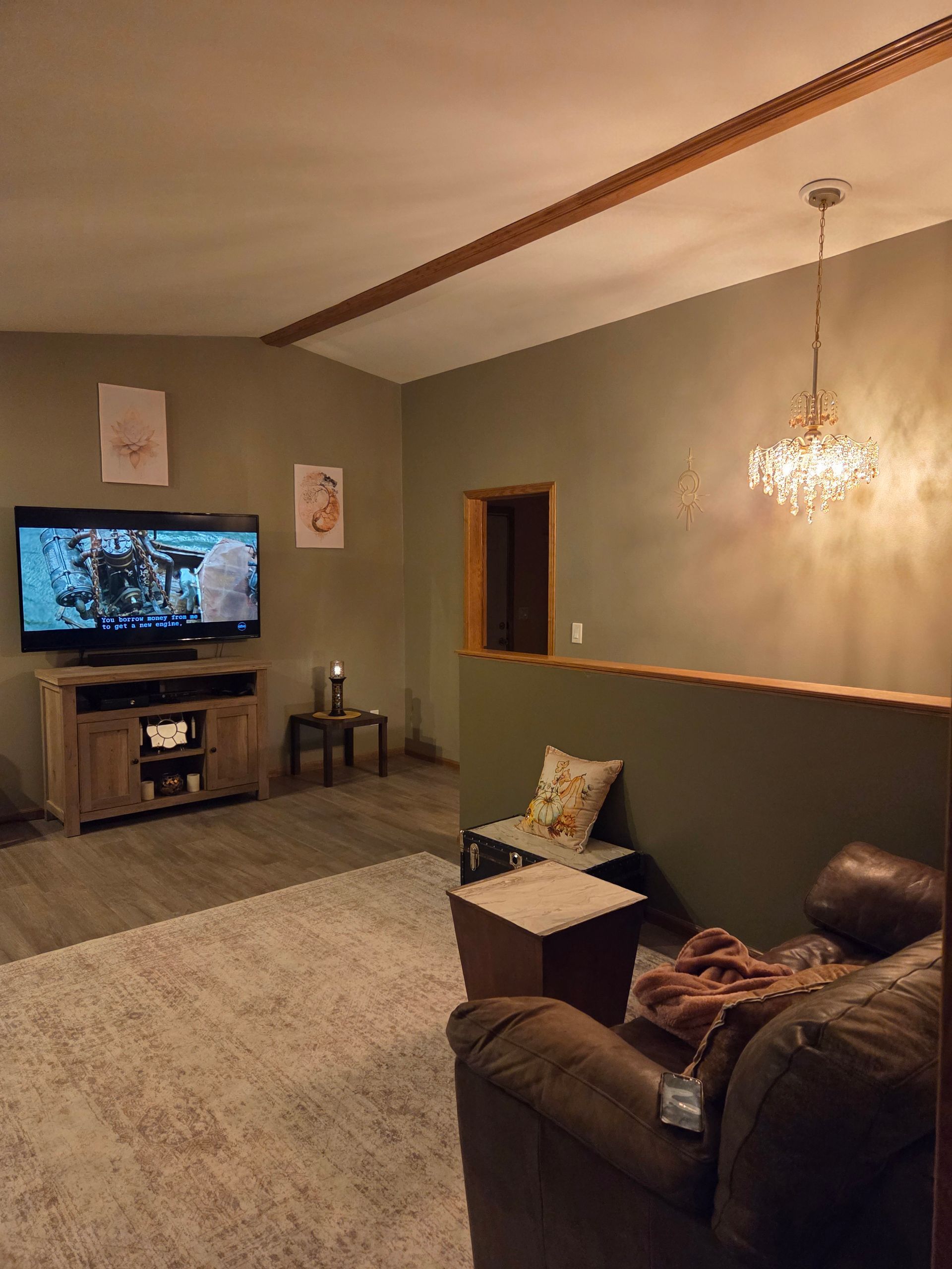 A living room with sage green walls, a large TV on a wooden stand, a light-colored rug, and a leather chair.