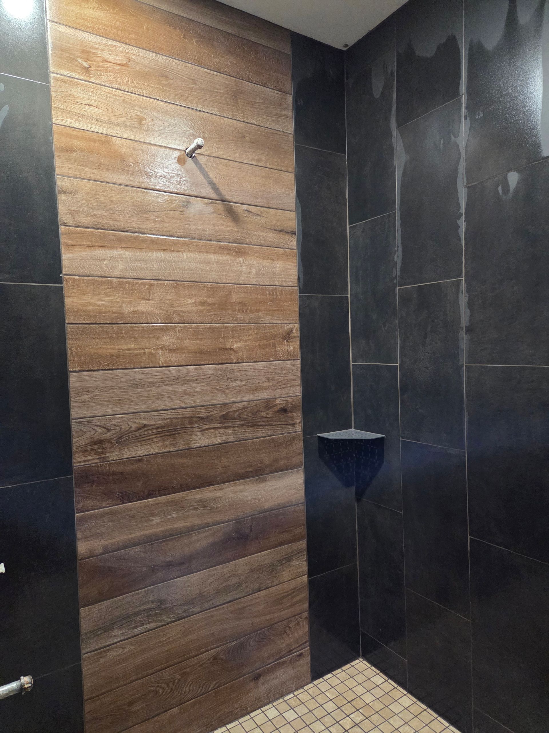 A shower stall with a textured, wood-look central panel flanked by smooth, dark charcoal-colored tiles.