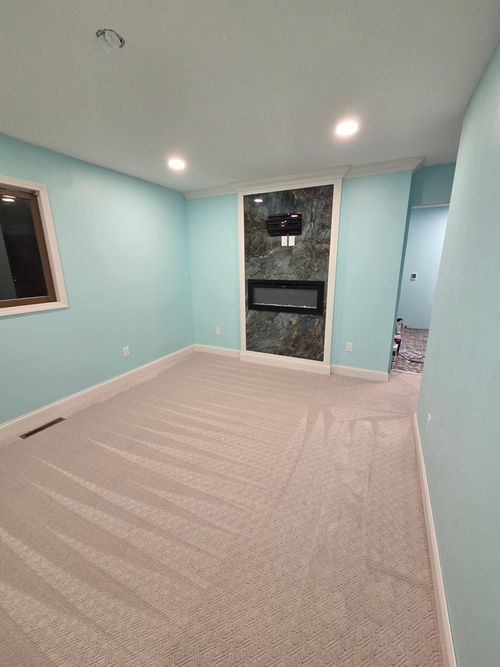 Empty room with light blue walls, tan carpet, recessed lighting, and a dark stone-tiled fireplace feature on one wall.