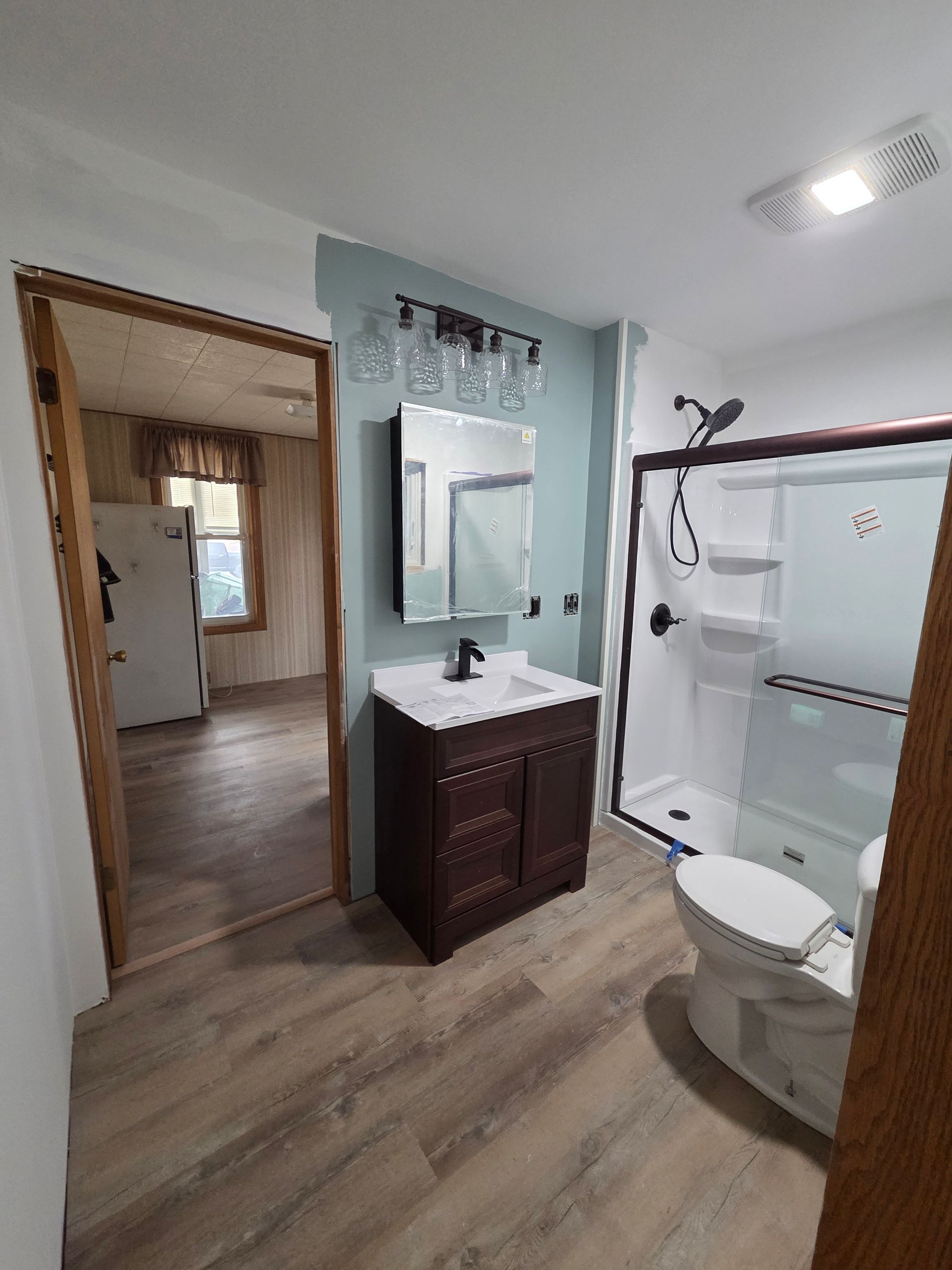 A bathroom with a dark wood vanity, a blue-green accent wall, a shower, and a white toilet, viewed from an open doorway.