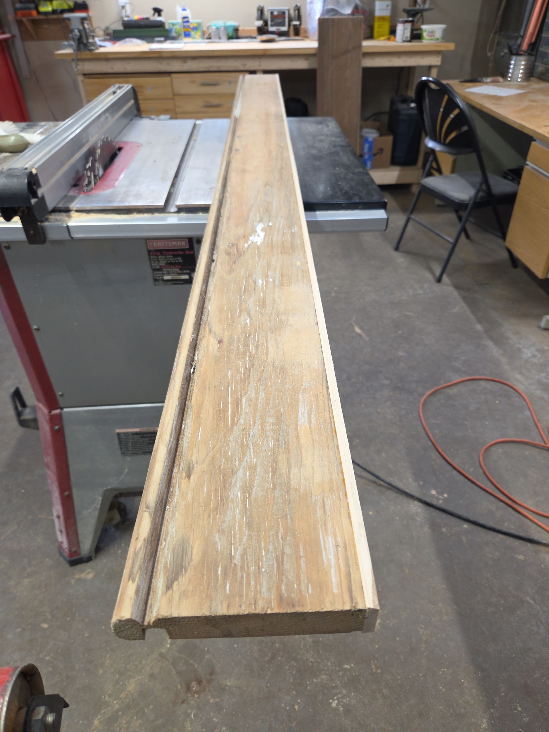 A wooden board with a rounded edge profile sits on a table saw in a woodworking shop.