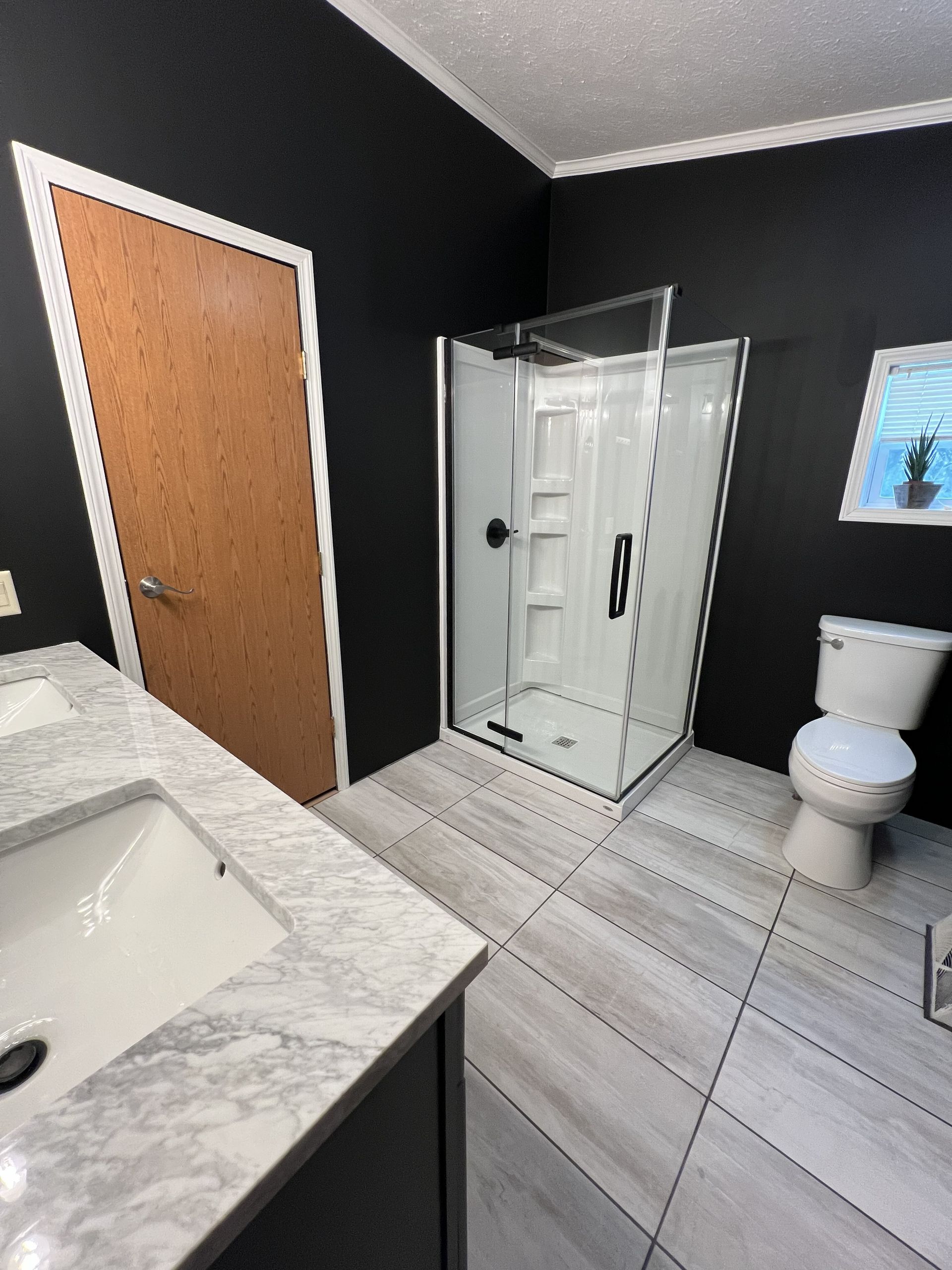 Bathroom with matte black walls, a light gray tile floor, a double vanity with a marble top, shower, and toilet.