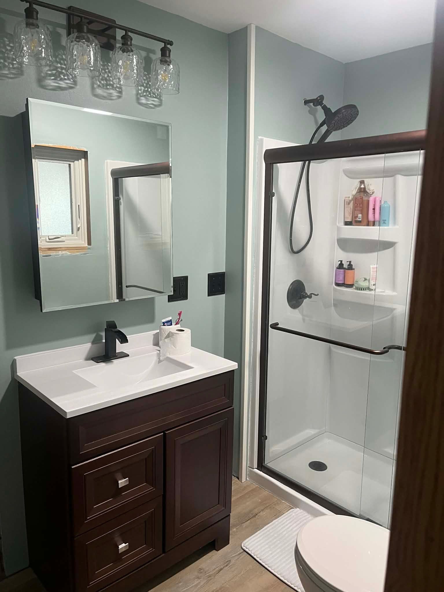 A bathroom featuring a dark wood vanity with a white countertop, a mirrored medicine cabinet, and a glass-enclosed shower.