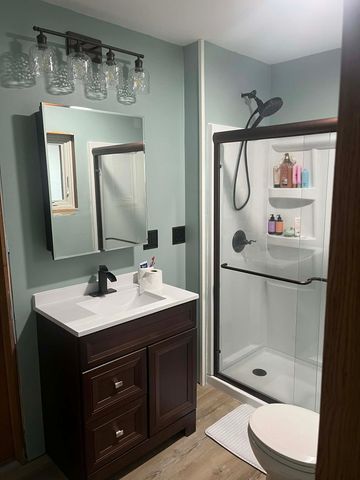 A bathroom with a dark wood vanity, white countertop, modern light fixture, and a glass-enclosed shower stall.