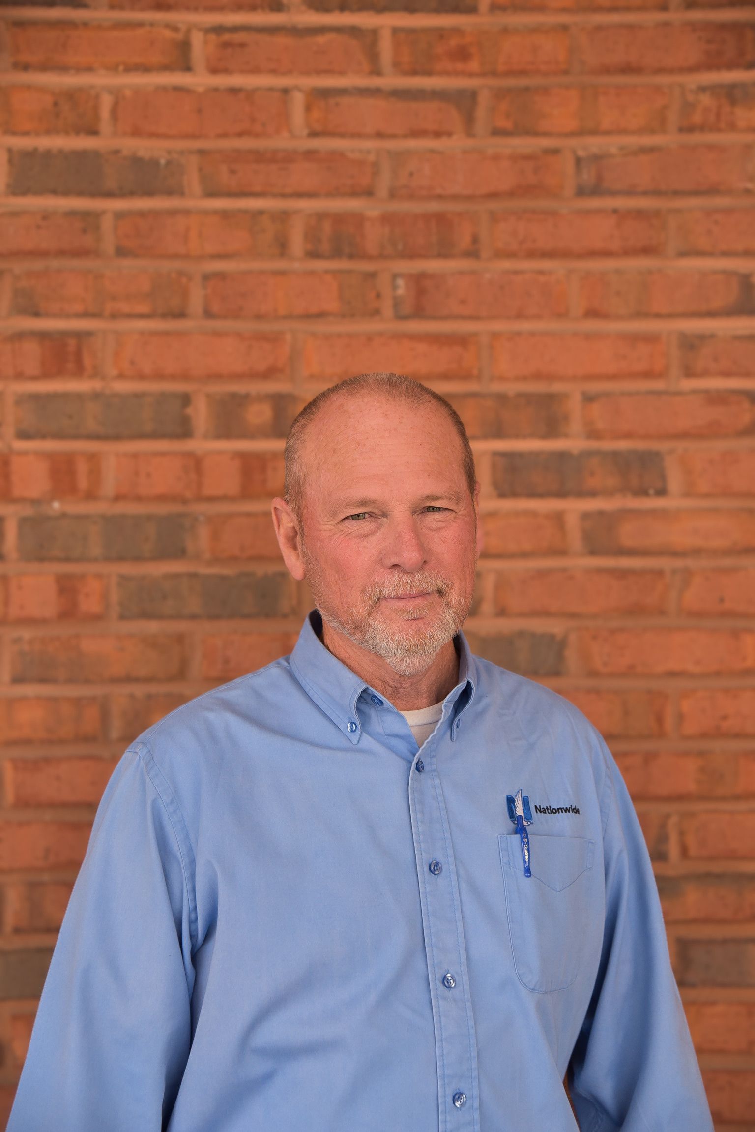 A man in a blue shirt is standing in front of a brick wall.