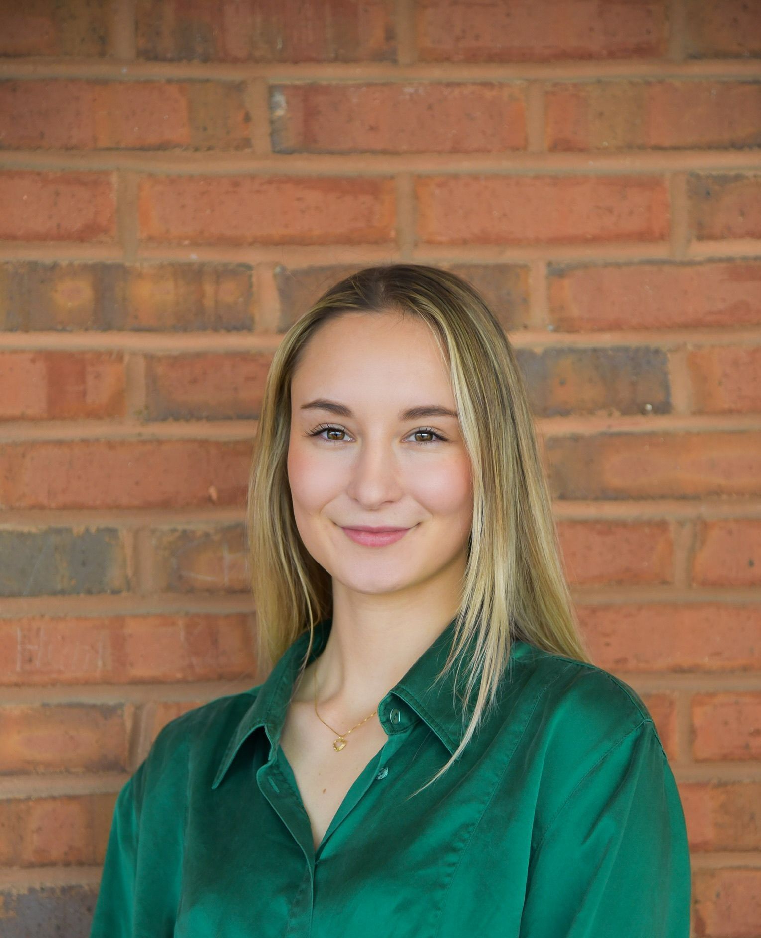 A woman in a green shirt is standing in front of a brick wall.