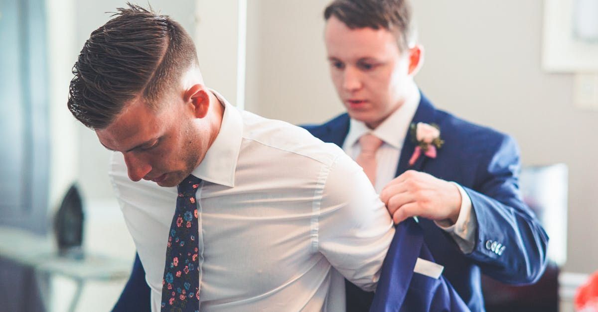 A man in a suit is helping another man get ready for his wedding.