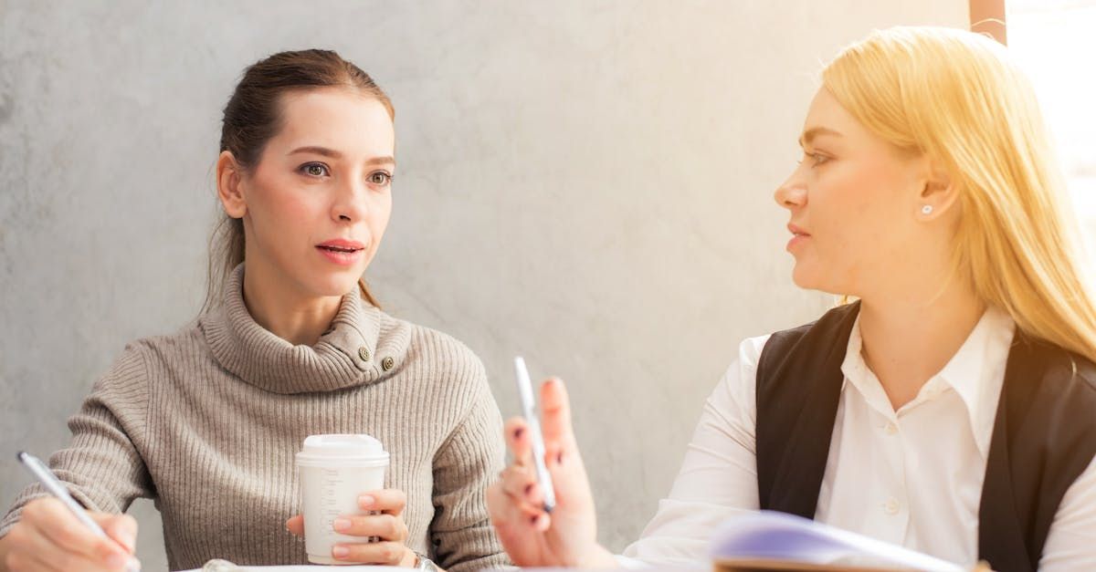 Two women are sitting at a table talking to each other.