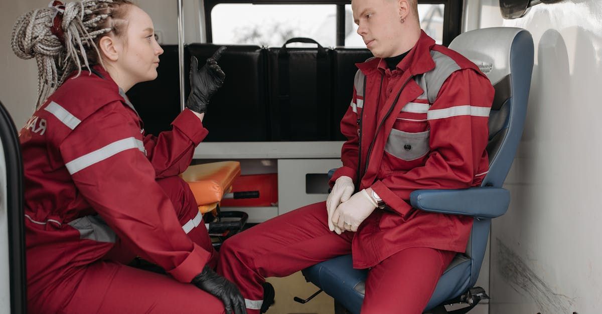 A man and a woman are sitting in an ambulance talking to each other.