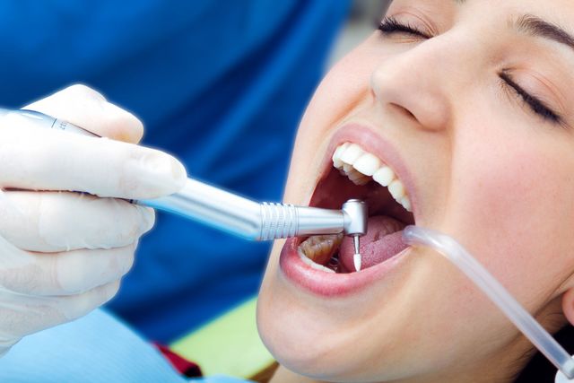 Un dentista utilizza uno strumento odontoiatrico e un aspiratore nella bocca aperta di un paziente durante una visita.