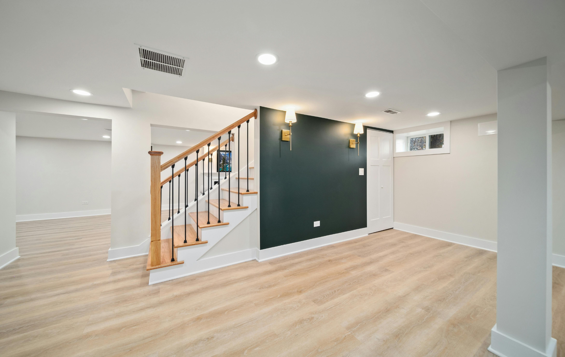 Basement interior with stairs, neutral colors, dark green accent wall, light wood flooring.