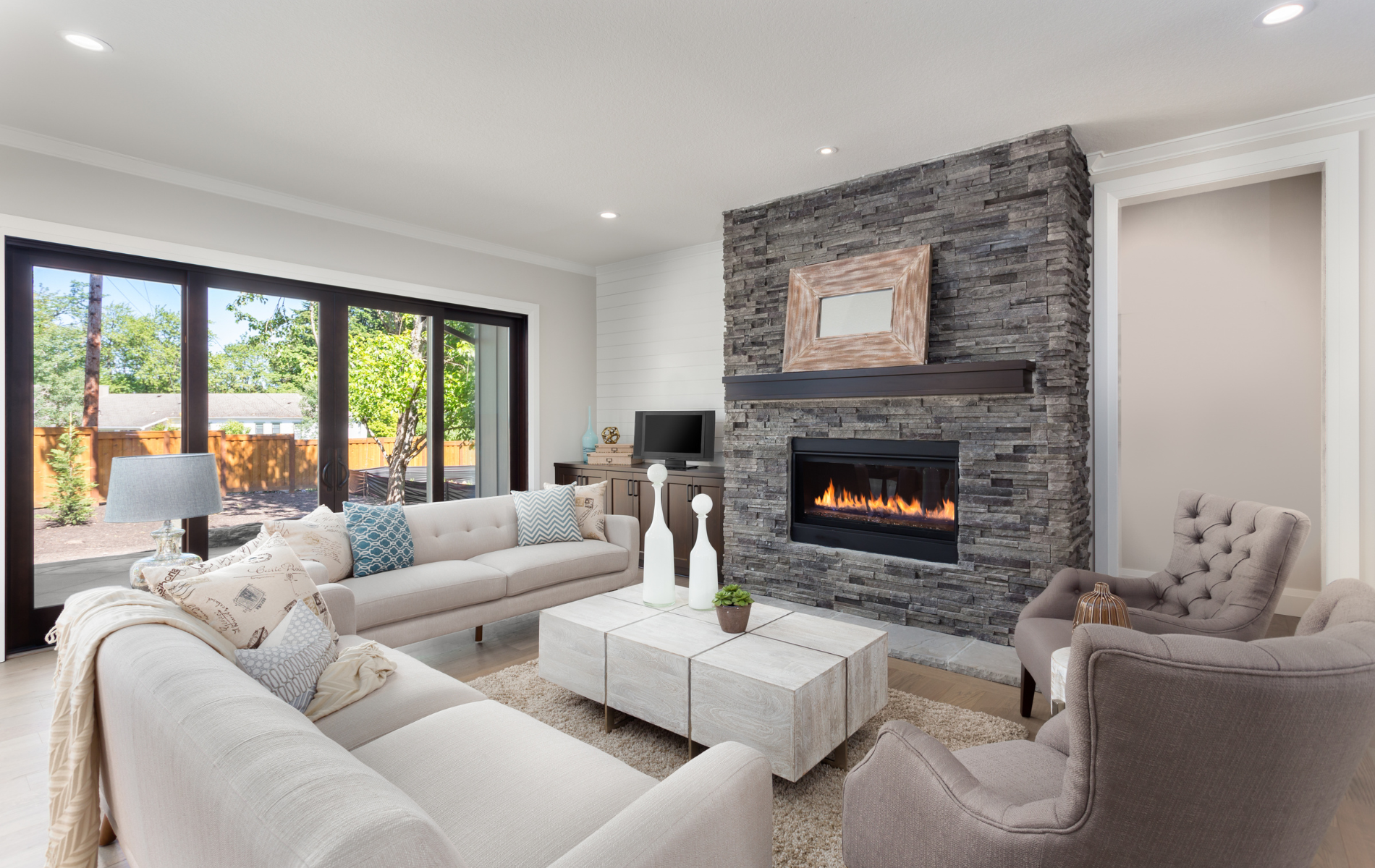 Living room with stone fireplace, couches, and large window overlooking a yard.