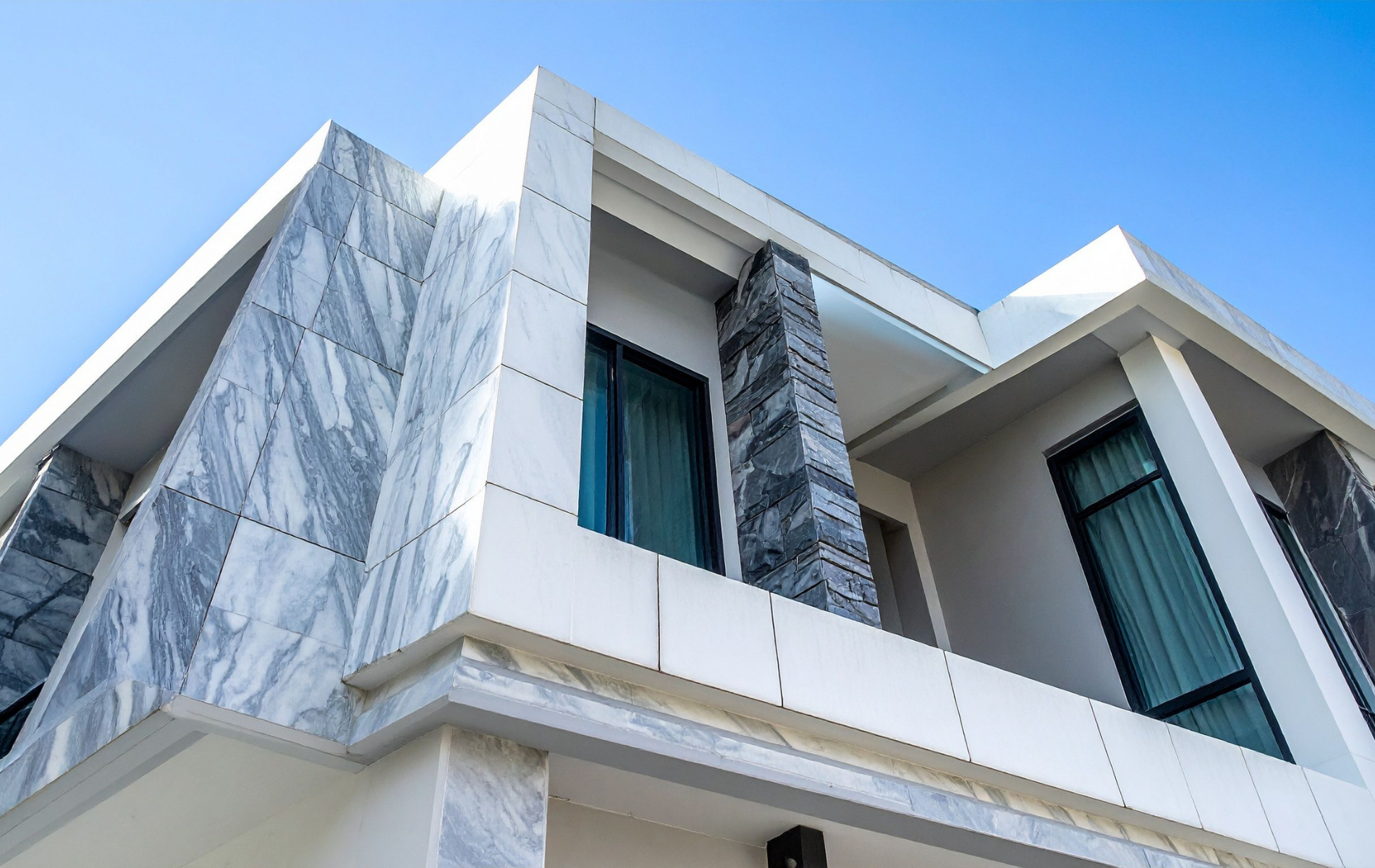 Modern building exterior with white and marble facade, windows, and a blue sky.