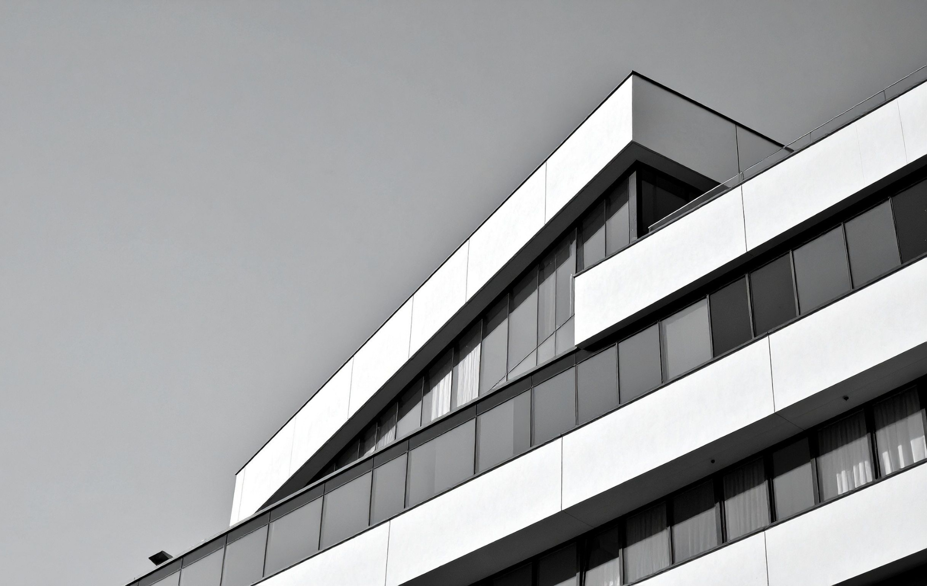 Modern building with angled roof and multiple rows of windows, in grayscale.