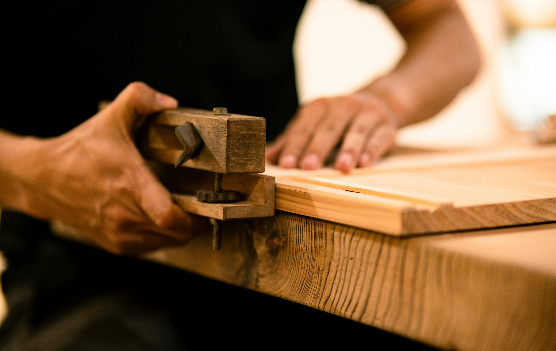 Hands using a wooden marking gauge on a wood board.
