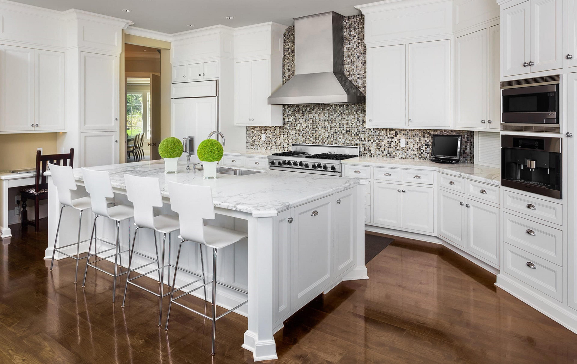 White kitchen with island, cabinets, and stainless steel appliances. Hardwood floors.