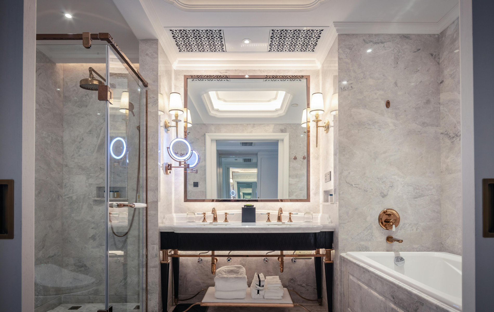 Elegant bathroom with marble walls, double sink, large mirror, and glass shower.