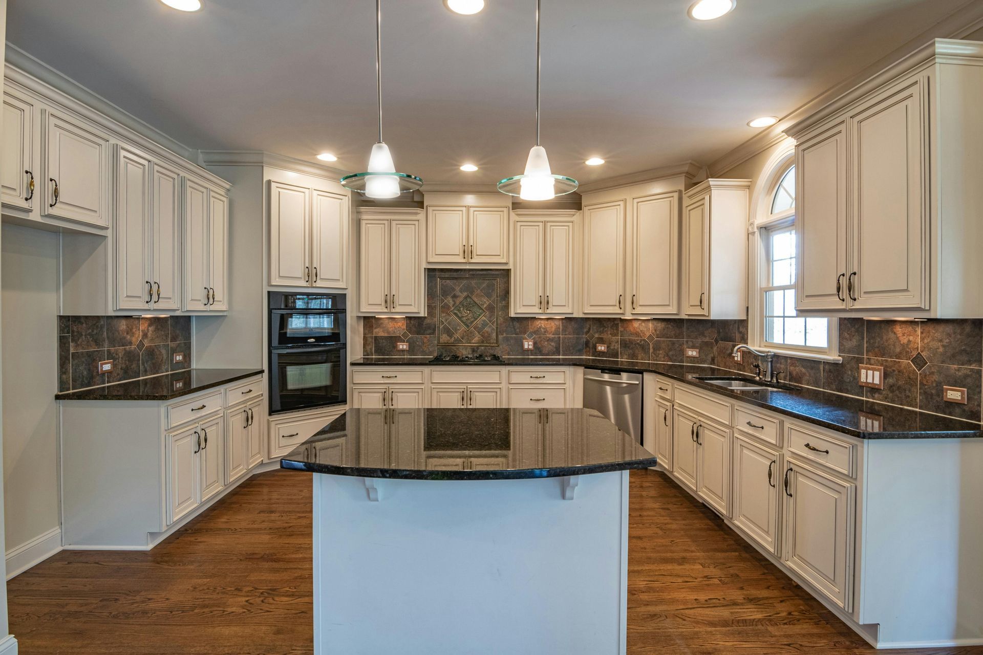 White kitchen with dark countertops, cabinets, and appliances. Wooden floor.
