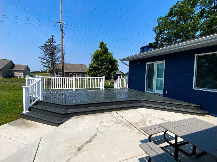 Backyard deck with white railing, blue house, and concrete patio under a clear sky