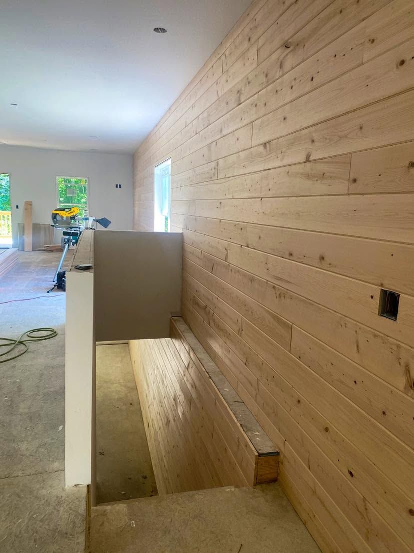 Long hallway under construction with wood-paneled wall, stair opening, and worker in the distance