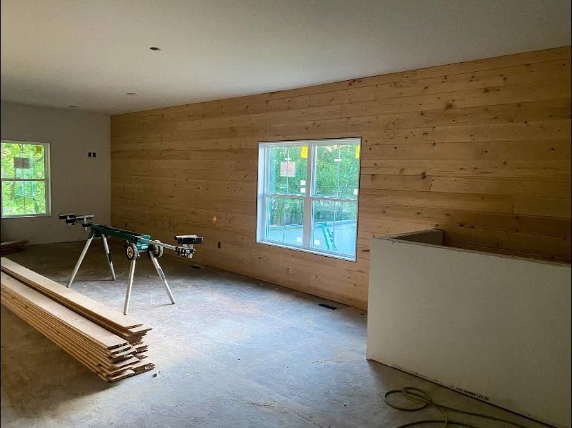 Partially finished room with wood-paneled walls, windows, and construction materials on the floor.