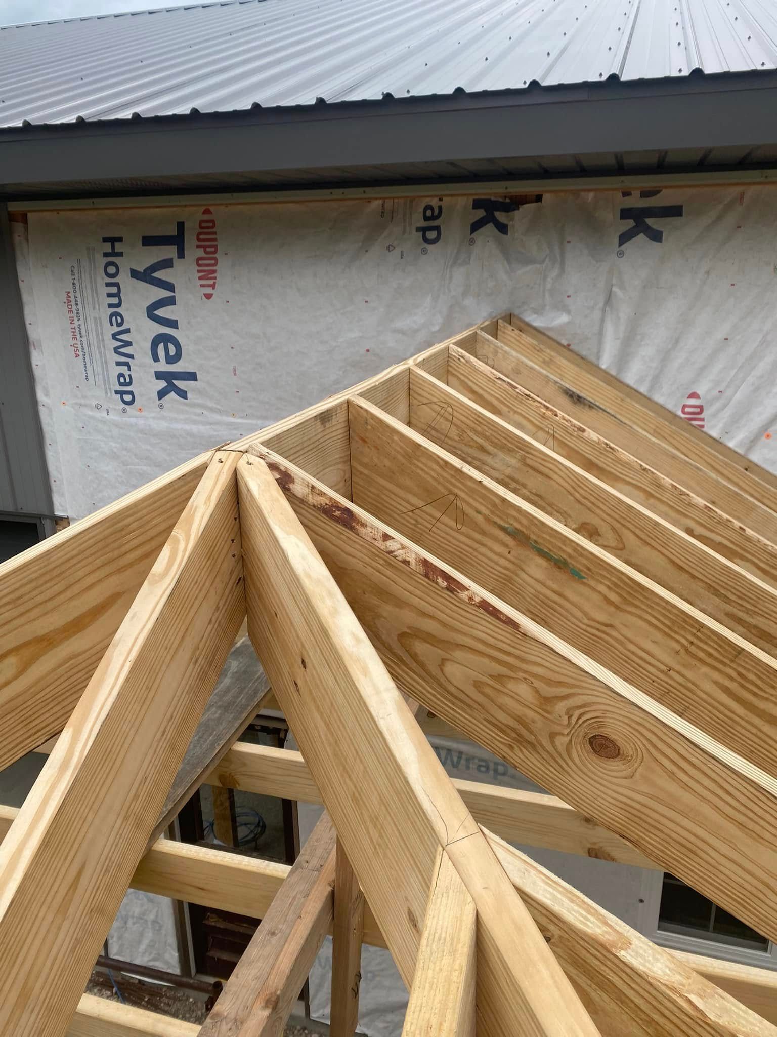 Wooden roof trusses under construction beside wrapped Tyvek house sheathing