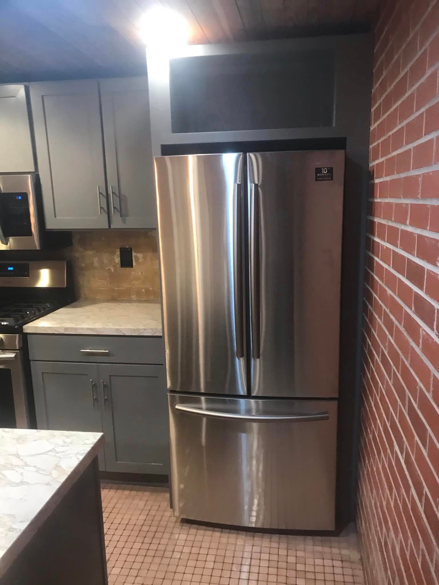 Kitchen counter with double sink, wooden countertop, dark cabinets, and exposed brick walls