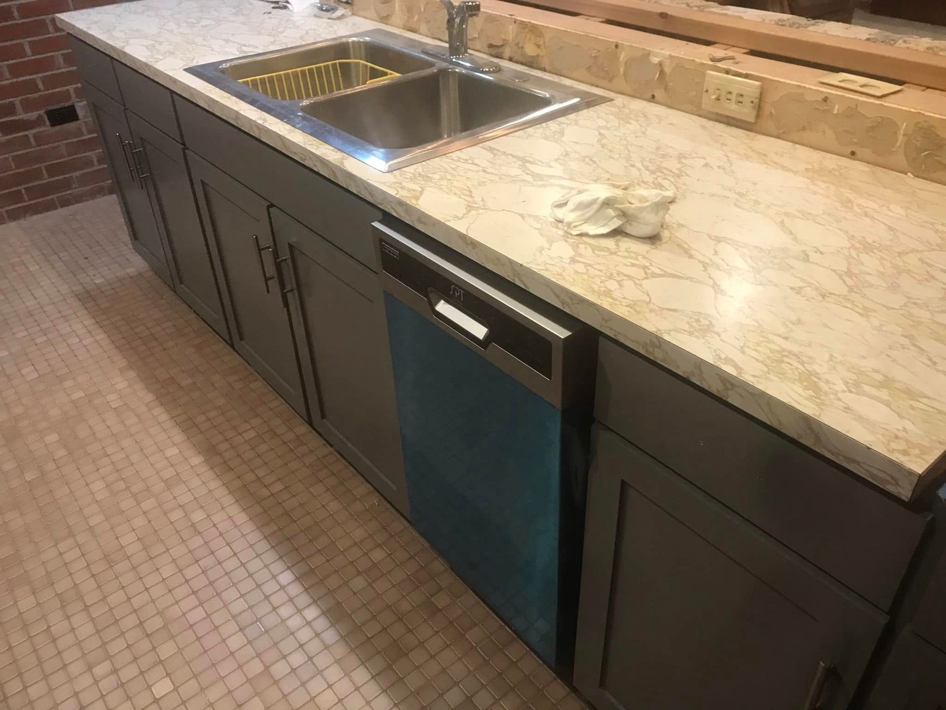 Modern kitchen island with stainless sink, beige stone countertop, and dark cabinets