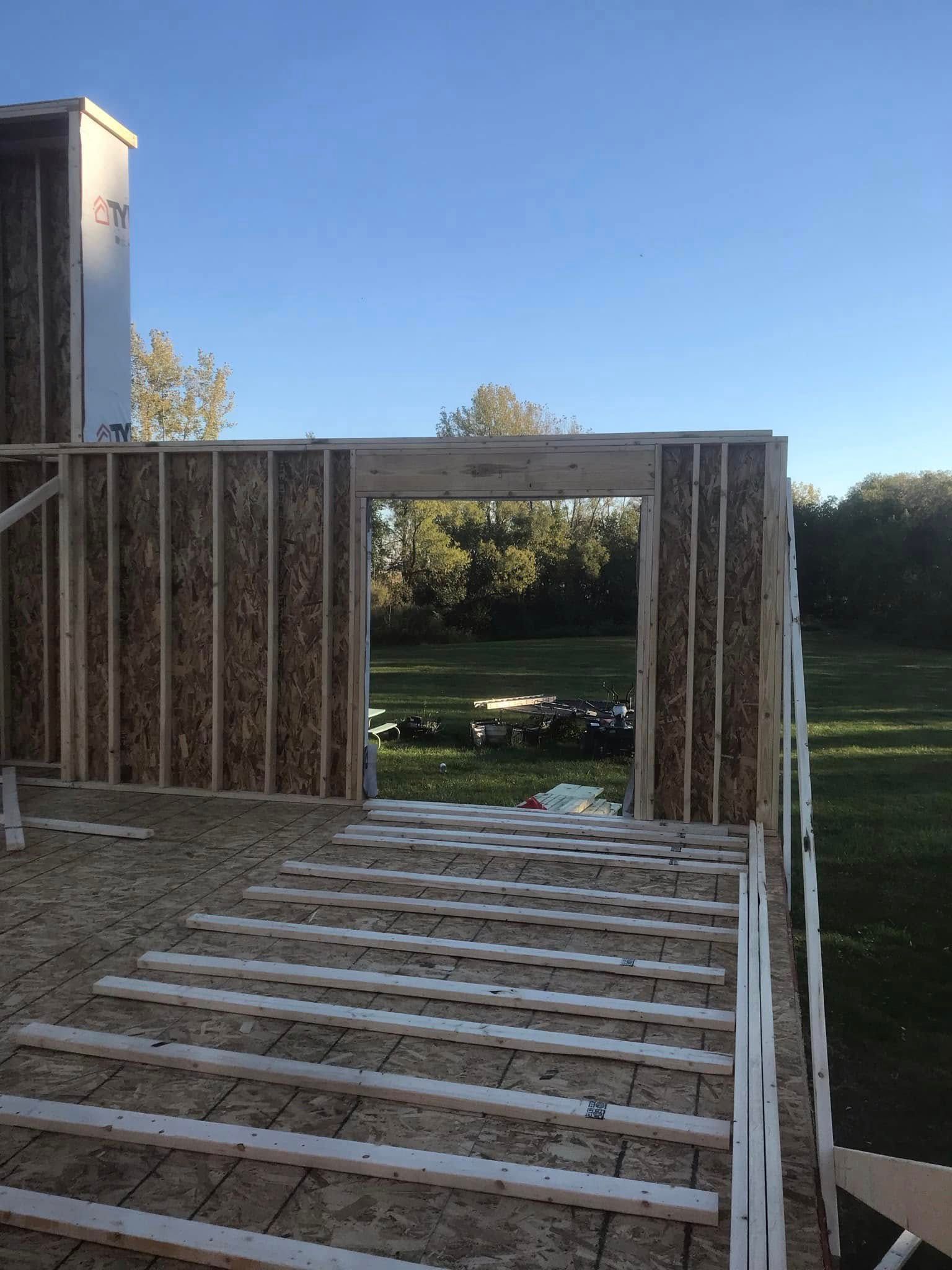 Partially built wooden deck frame beside a house, overlooking a grassy yard and trees.