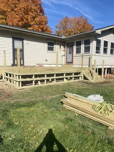 Backyard wooden deck with railing and steps beside a light gray house under a blue sky