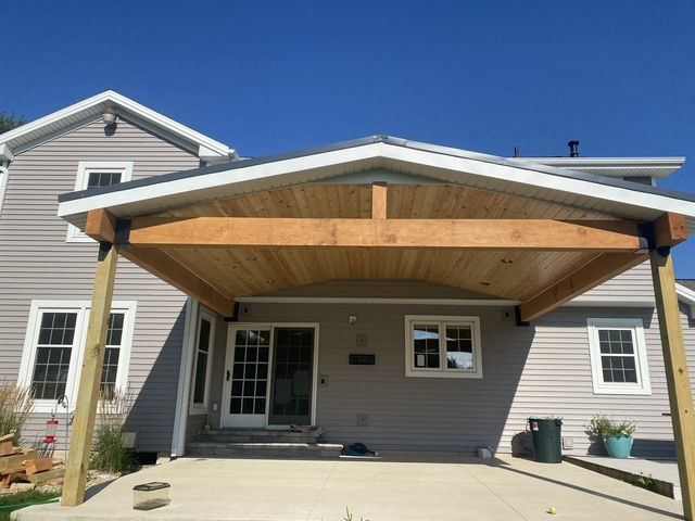 Covered front porch with wood ceiling and gray siding on a house under a blue sky