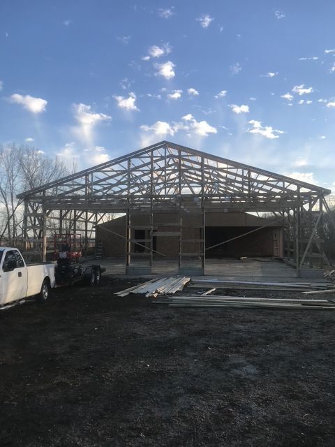 Partially built porch roof under construction with exposed rafters, ladders, and support posts beside a house