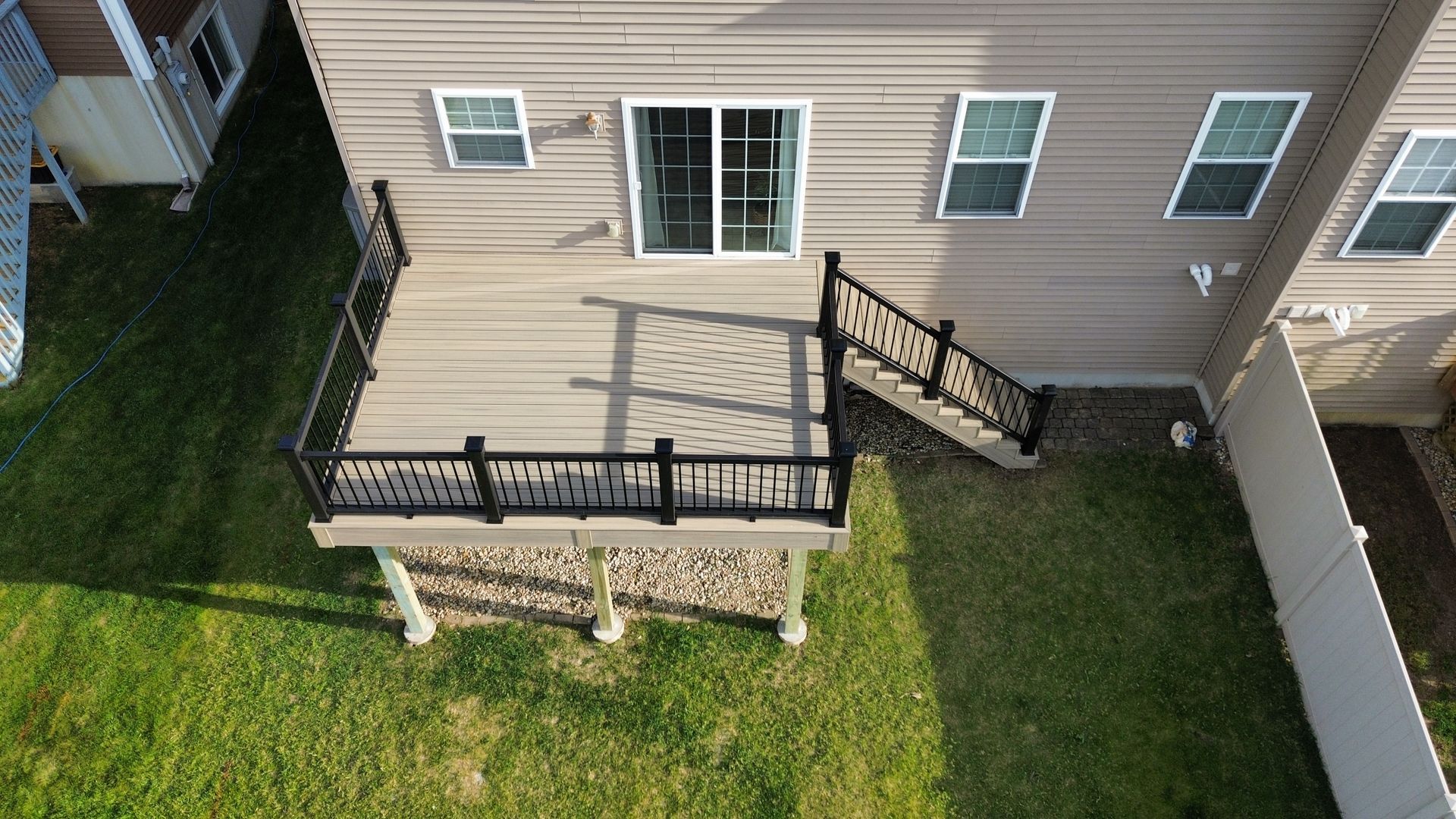 Backyard concrete patio with wooden deck steps beside a white house under a blue sky