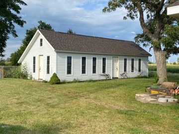 White house exterior with sloped roof, metal ladder, and gravel path beside a grassy yard.