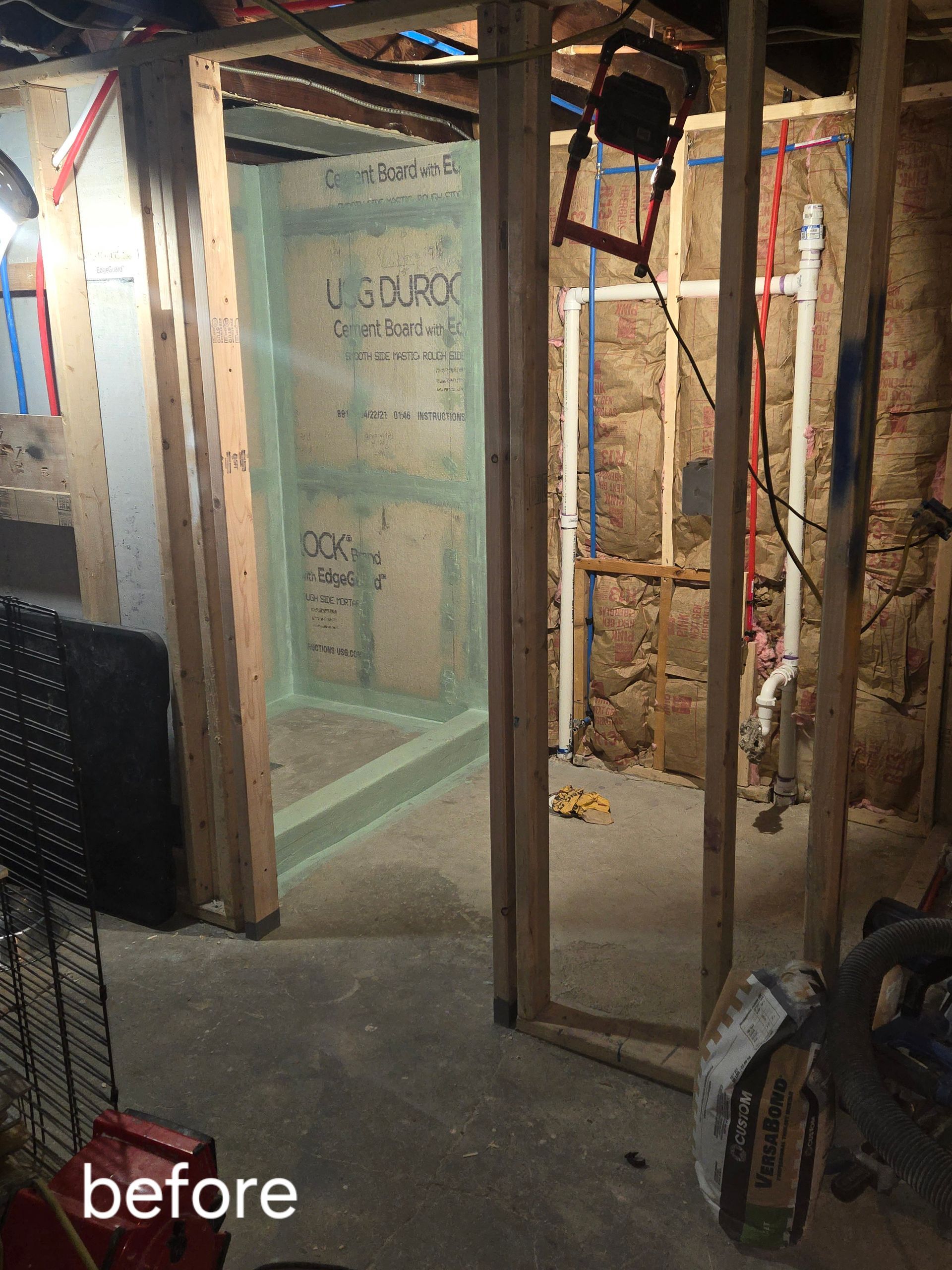 Framed-out basement bathroom renovation in progress; unfinished walls, shower stall with Durock, exposed plumbing.