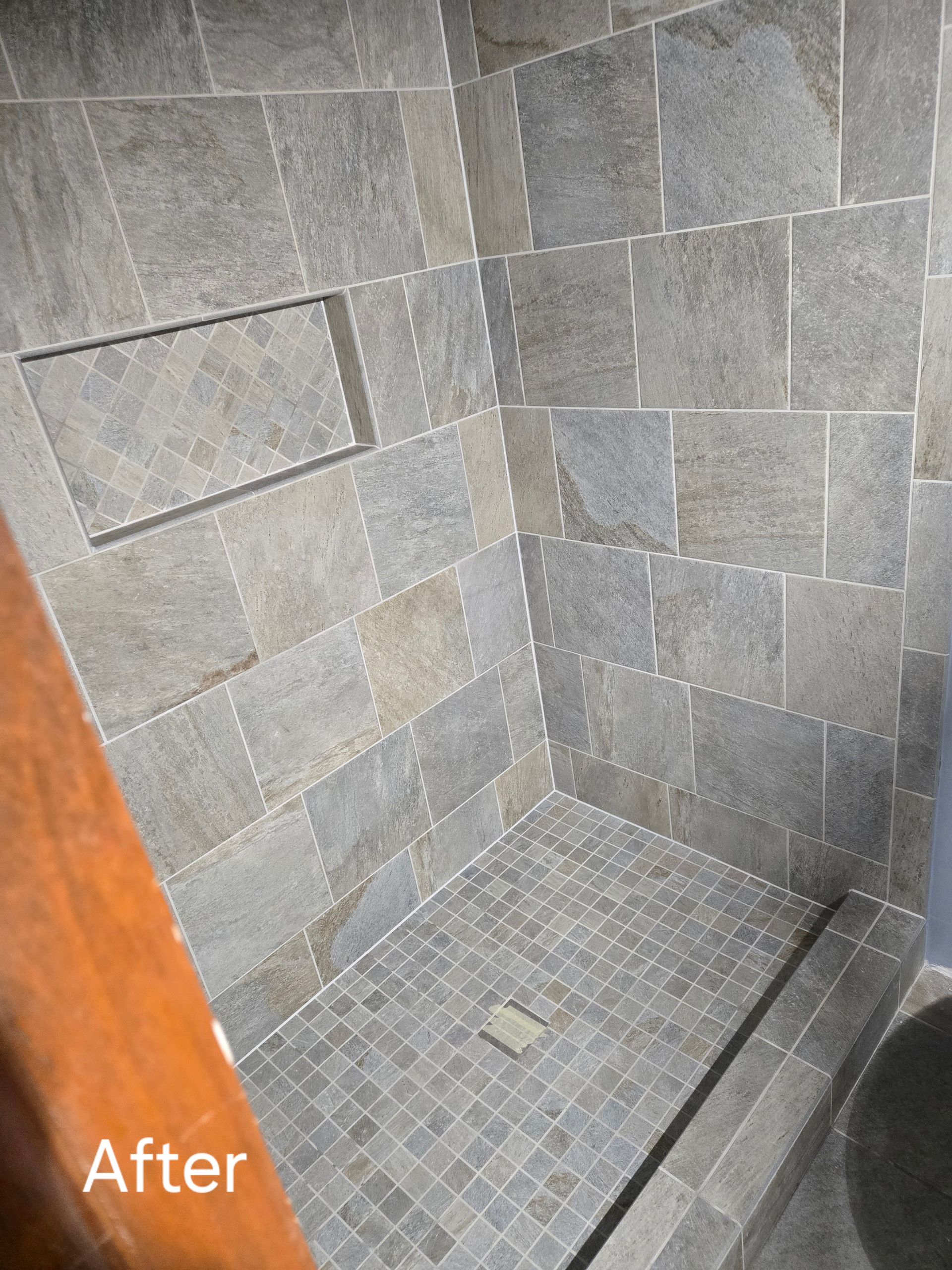 Shower with gray tile walls, mosaic tile floor, and a built-in shelf.