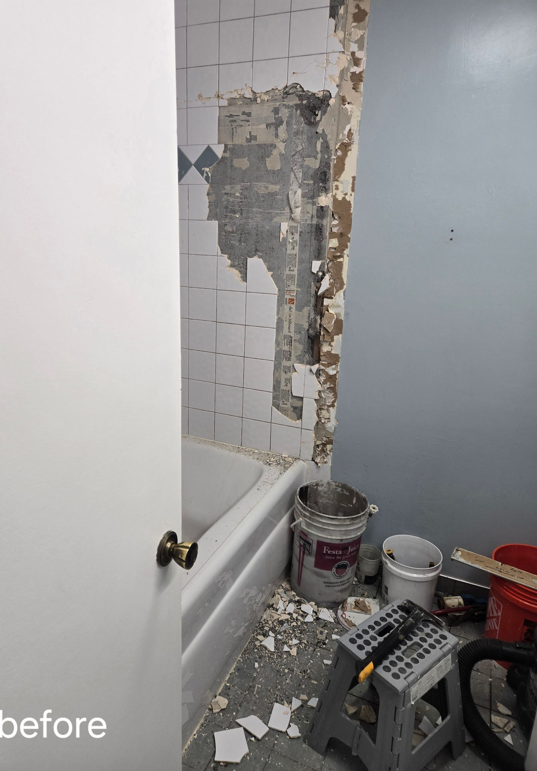 Bathroom renovation: Damaged tile wall, partially exposed, next to blue wall and white bathtub. Debris on floor.