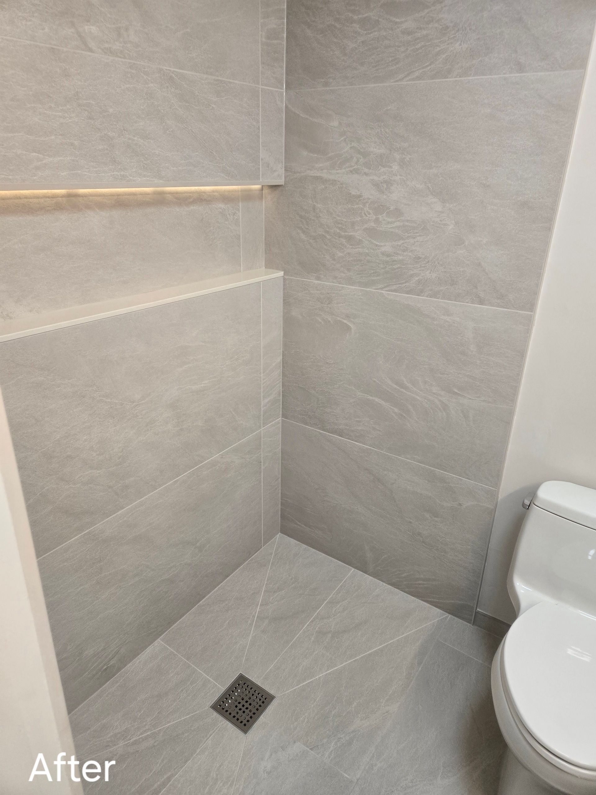 Modern gray tiled shower with a toilet on the right. A linear drain is centered on the floor.