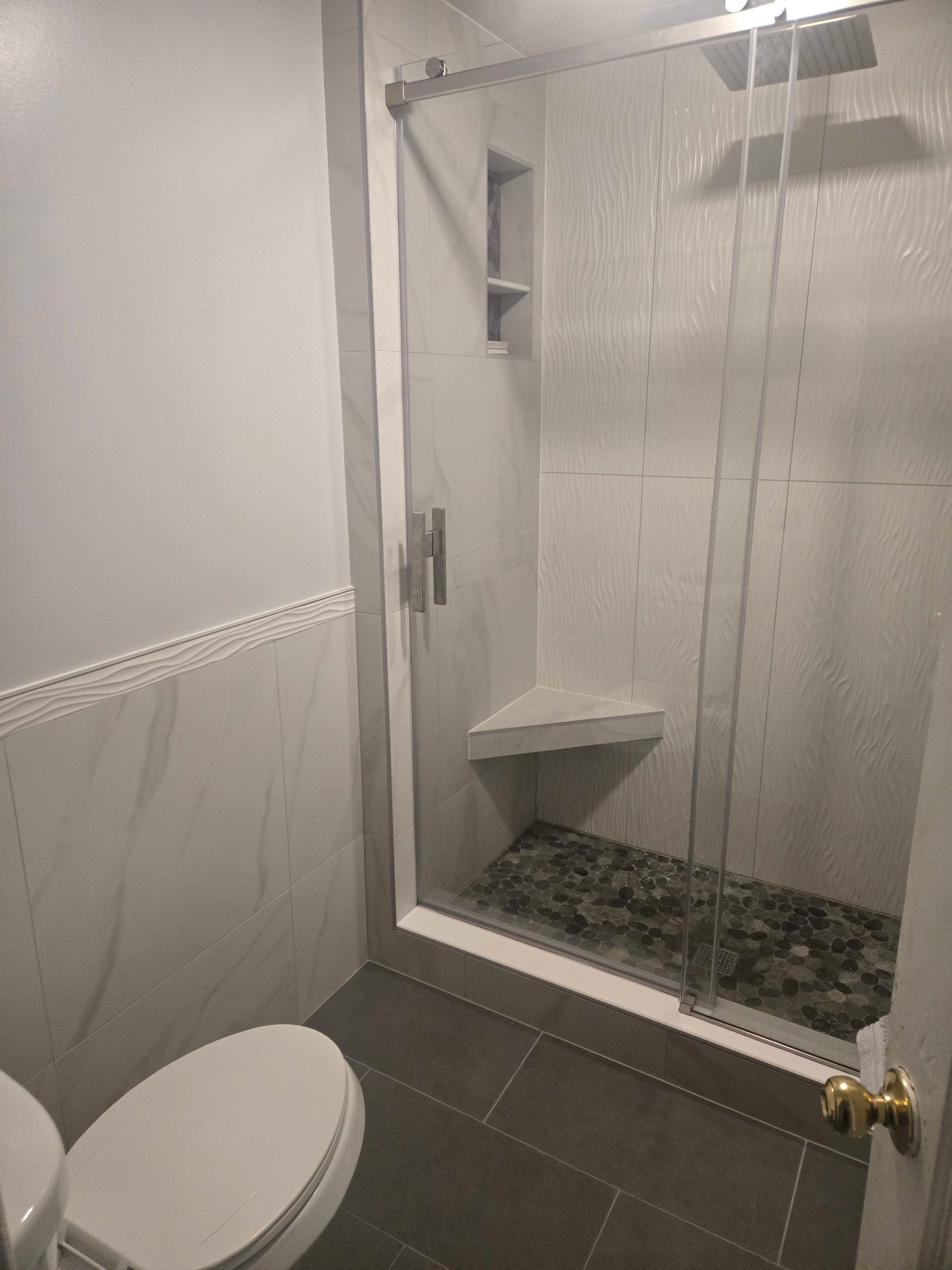 Bathroom with a tiled shower, glass door, toilet, and gray flooring.