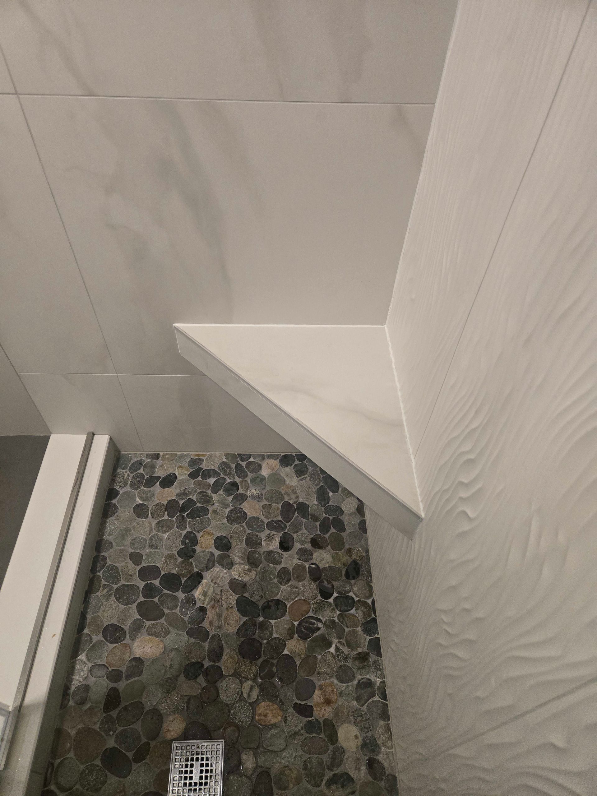 Shower interior with pebble floor, white walls, and a built-in shelf.