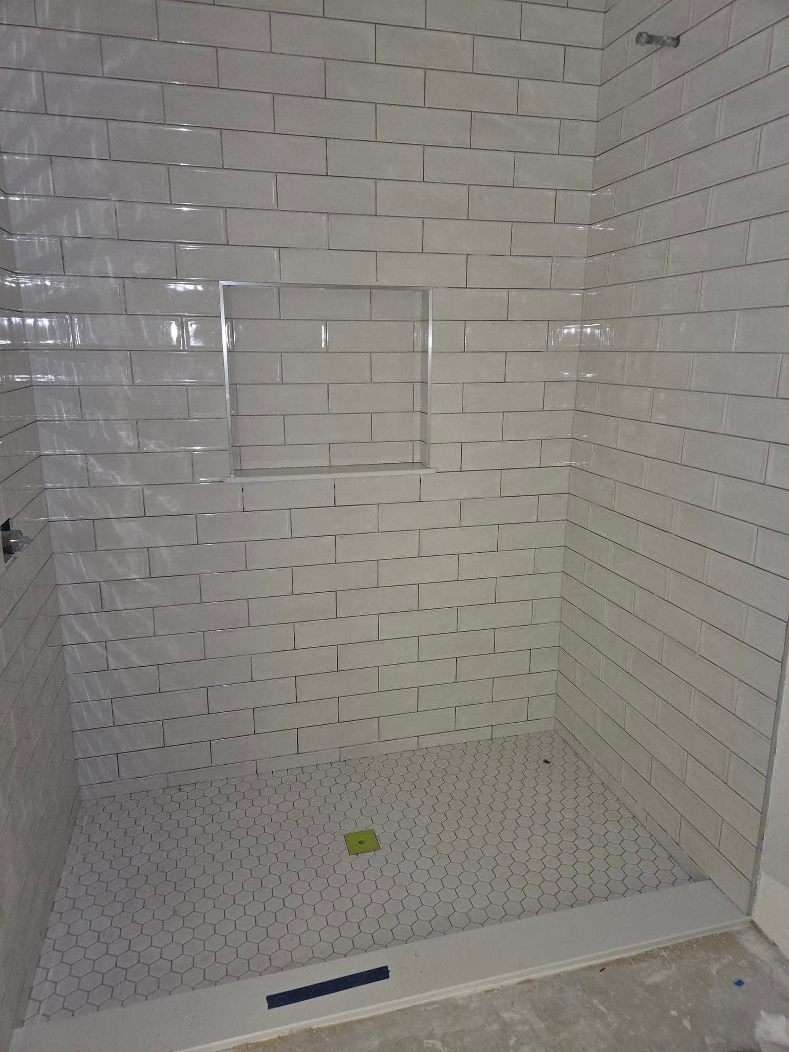 Tiled shower stall with a built-in shelf and floor drain. The walls are light-colored, with a textured design.