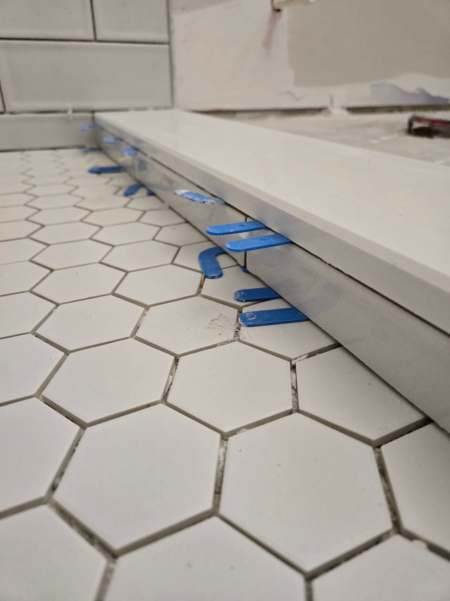 White countertop secured with blue clips over white hexagon tiles, during construction.