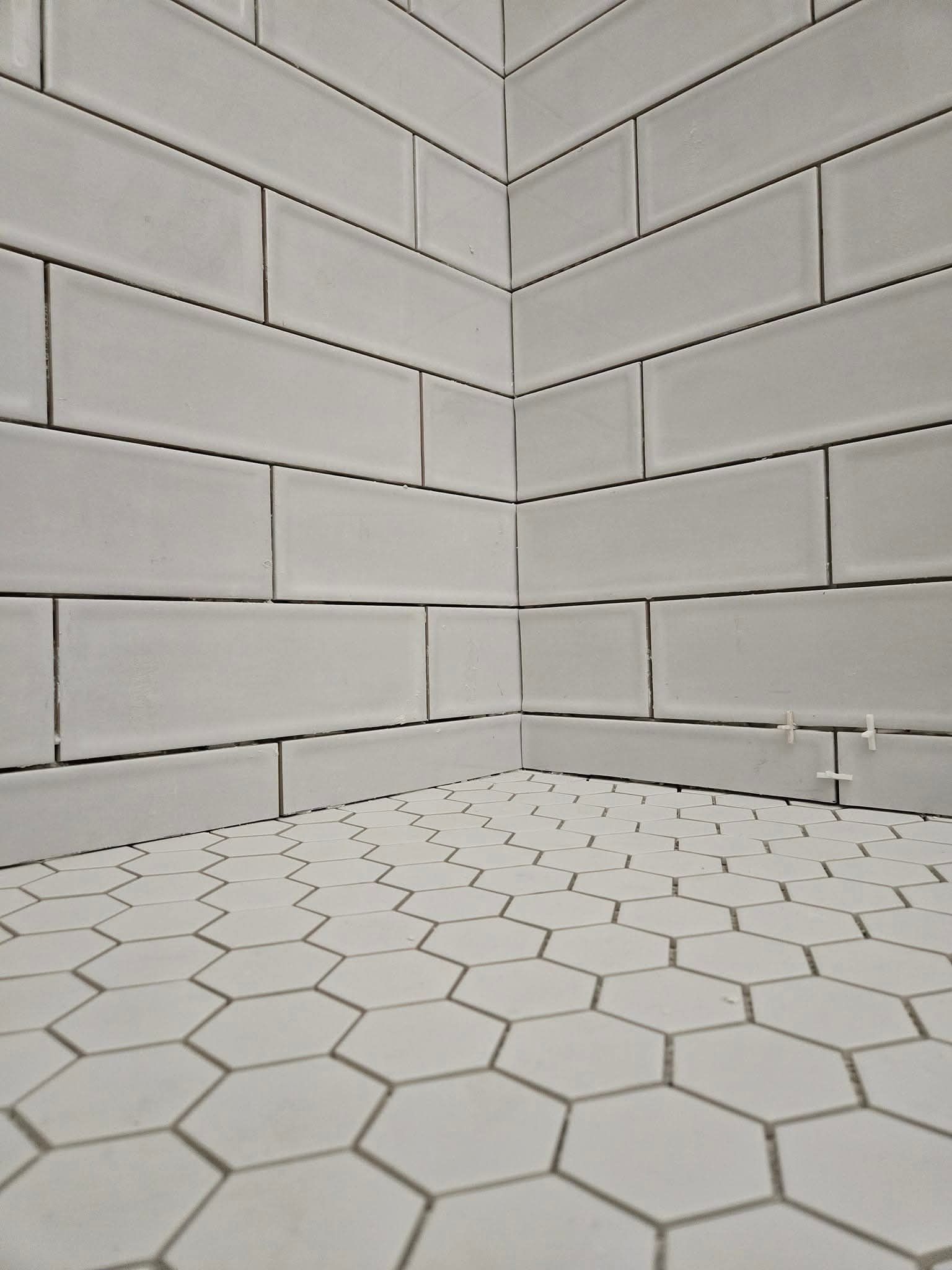 White tiled bathroom corner: subway tile walls meet hexagon tile floor.