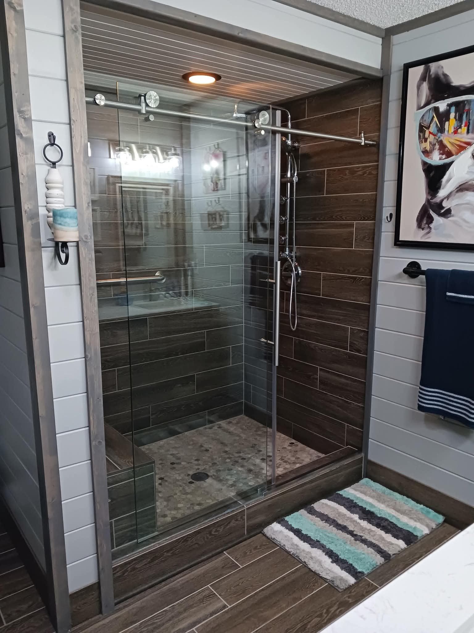Shower with glass door and brown tile, gray walls, and a small rug.