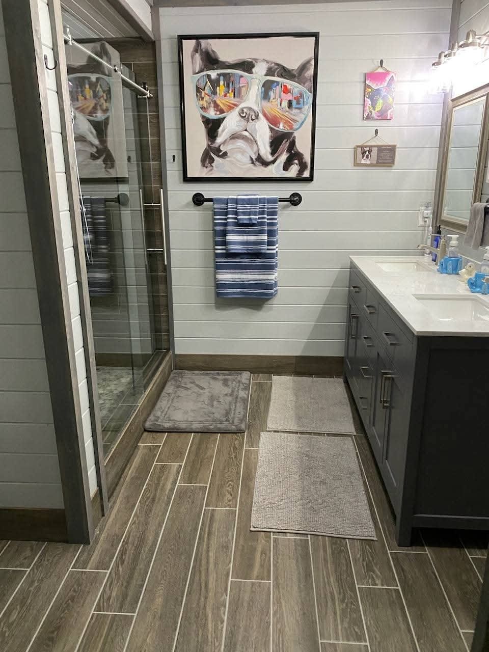Bathroom with gray vanity, dog art, glass shower, and wood-look tile.