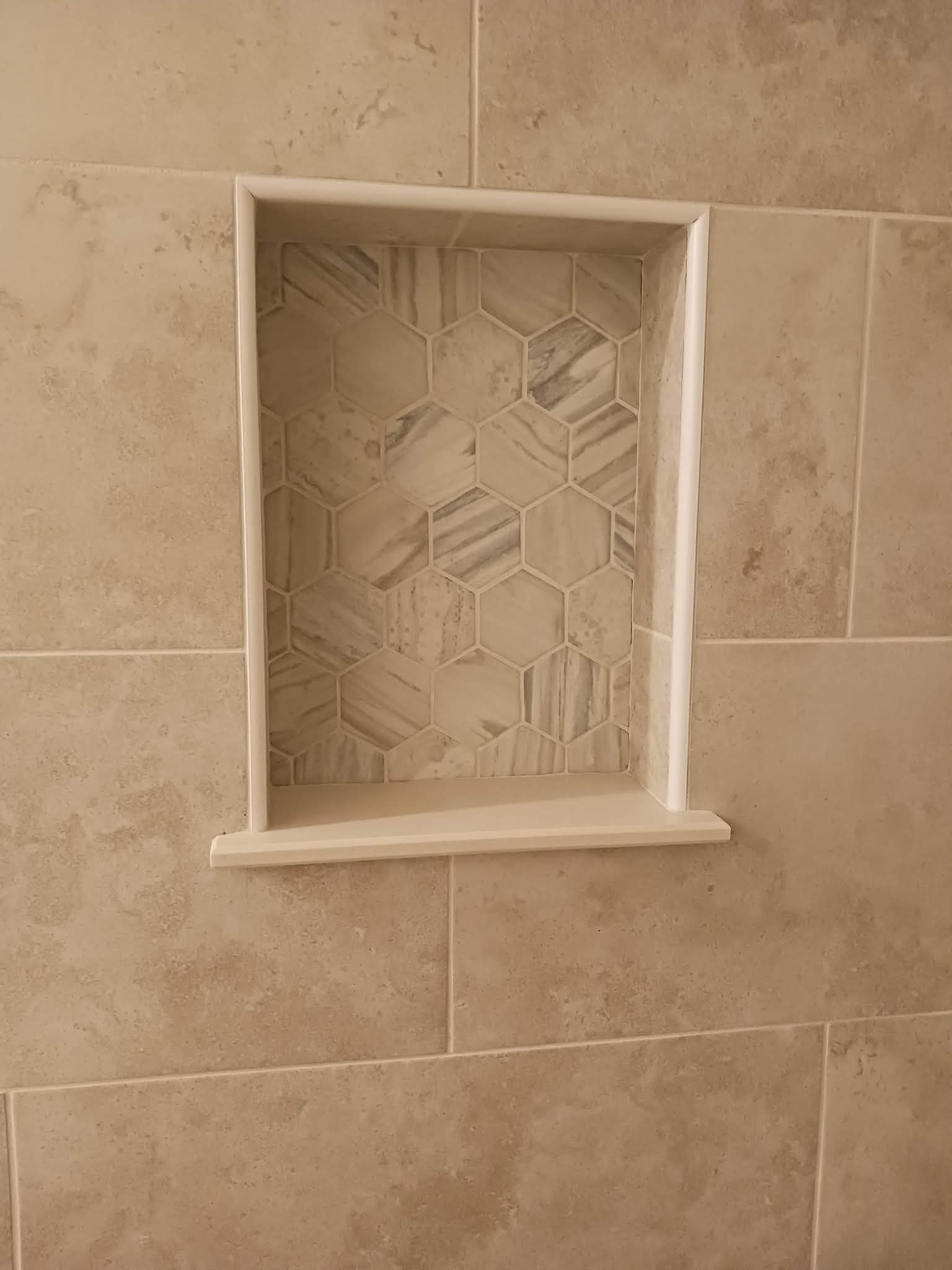 Recessed shower niche with patterned hexagonal tiles and a stone shelf. Light brown tiles surround the niche.